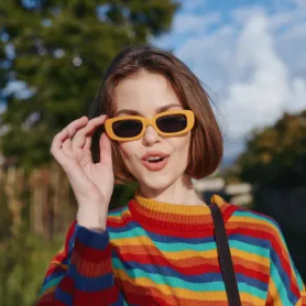 Woman, young woman, striped sweater, yellow sunglasses, smiling: early twenties female with short brown hair in colorful knit jumper and retro shades, playful surprised expression, casual shoulder