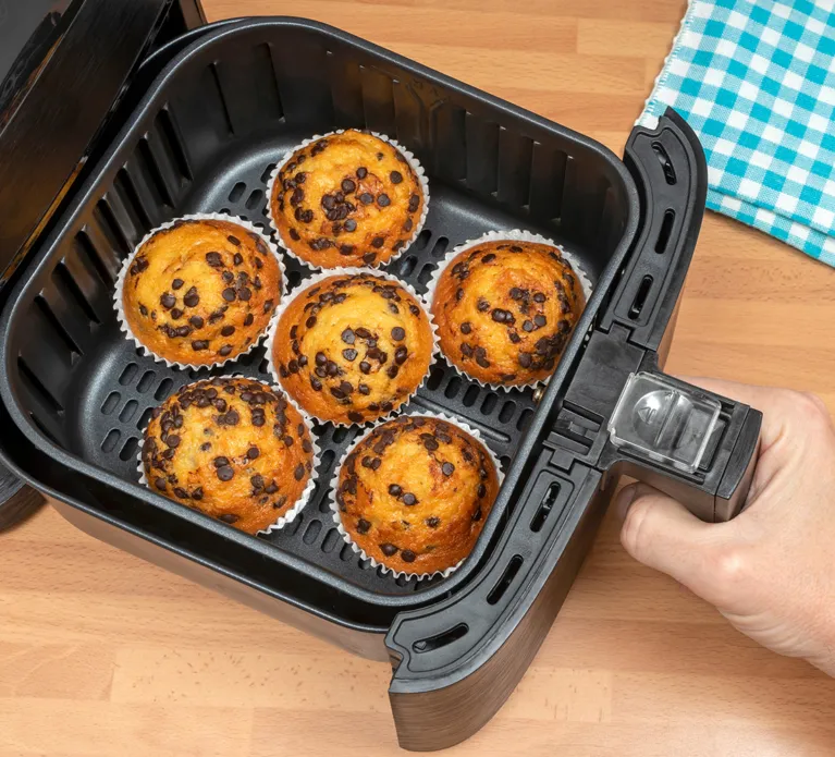 Top view of a hand baking homemade chocolate chips muffins in an air fryer.
