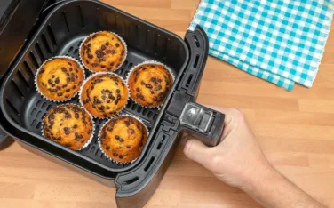 Top view of a hand baking homemade chocolate chips muffins in an air fryer.