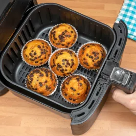 Top view of a hand baking homemade chocolate chips muffins in an air fryer.