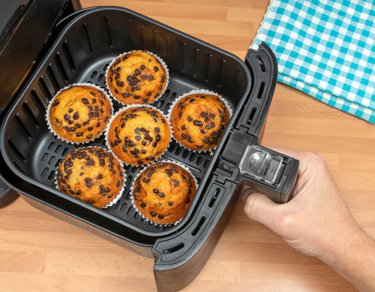 Top view of a hand baking homemade chocolate chips muffins in an air fryer.