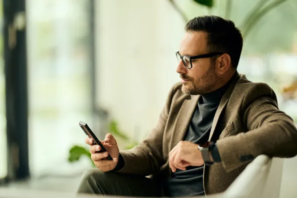 A professional man in a blazer uses a smartphone in a modern indoor lounge with a calm, focused vibe.